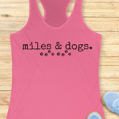 Pink tank top with 'miles & dogs.' text on a wooden surface
