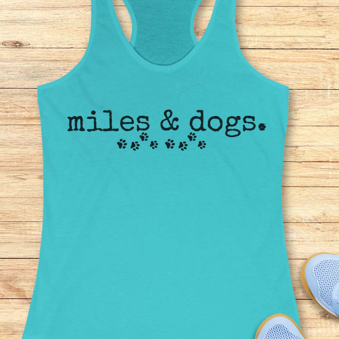 Turquoise tank top with 'miles & dogs.' text on a wooden surface
