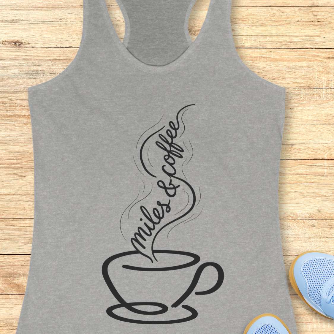 Gray tank top with a coffee cup and text  miles and coffee design on a wooden surface