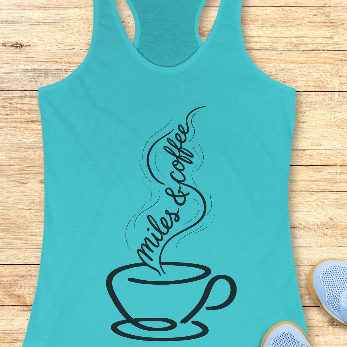 Turquoise tank top with a coffee cup design and text miles and coffee on a wooden surface