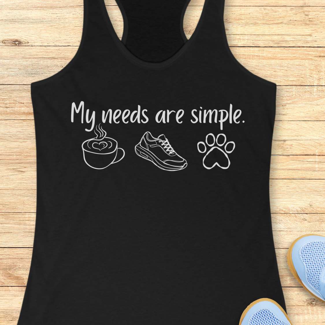 Black tank top with white text My needs are simple, and graphics on a wooden surface
