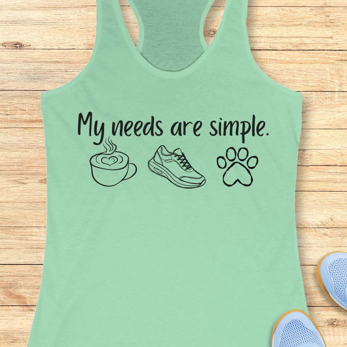 Mint green tank top with text My needs are simple, and graphics on a wooden surface