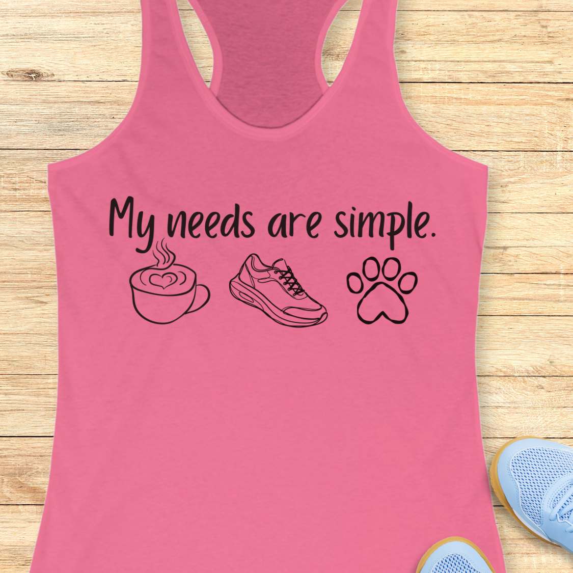 Pink tank top with text My needs are simple, and graphics on a wooden surface