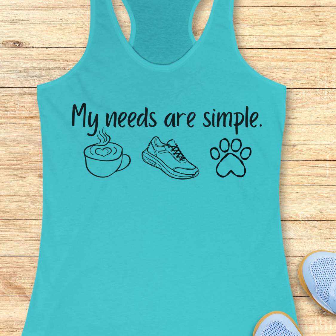 Turquoise tank top with text My needs are simple, and graphics on a wooden surface