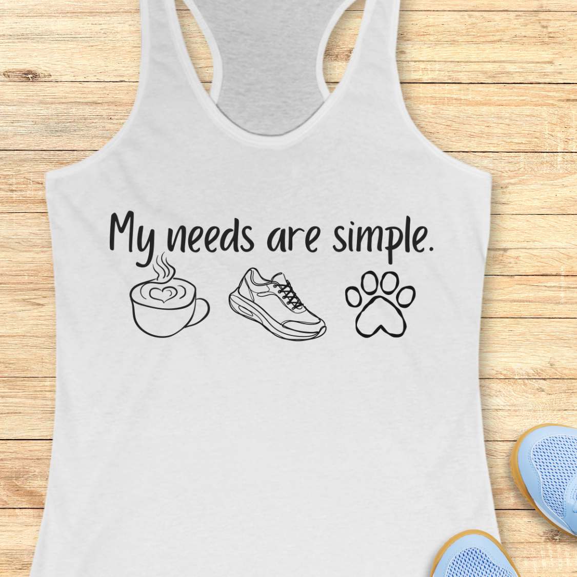 White tank top with text My needs are simple, and graphics on a wooden surface