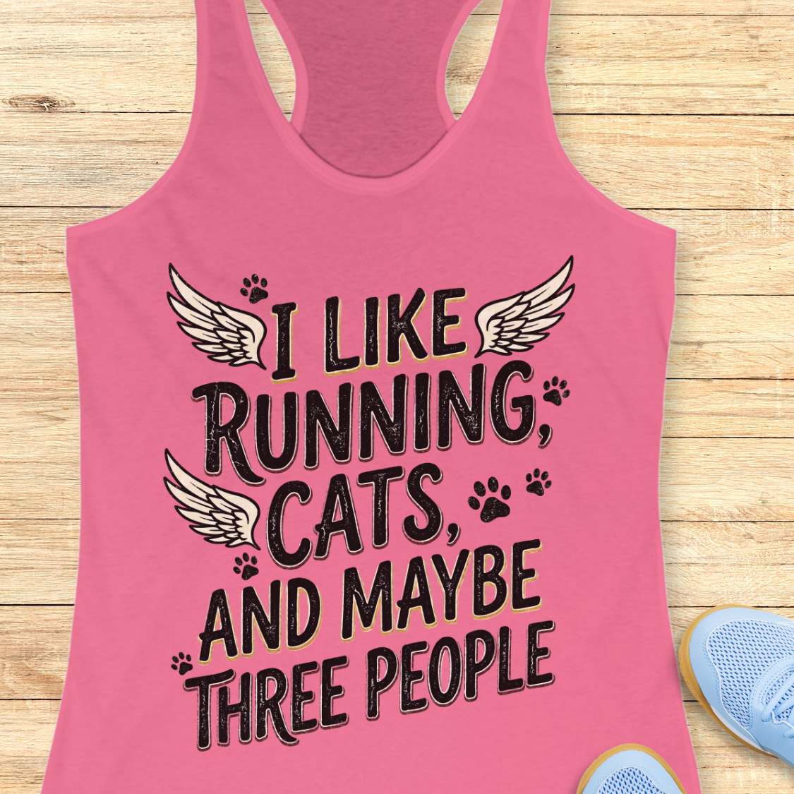Pink tank top with text 'I like running, cats, and maybe three people' on a wooden surface.
