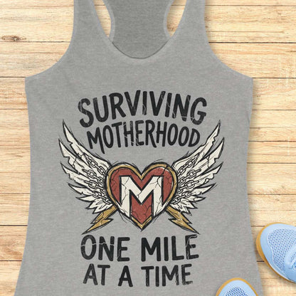 Gray tank top with 'Surviving Motherhood One Mile At A Time' design on a wooden surface