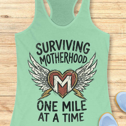 Green tank top with 'Surviving Motherhood One Mile at a Time' text and heart design on a wooden surface.