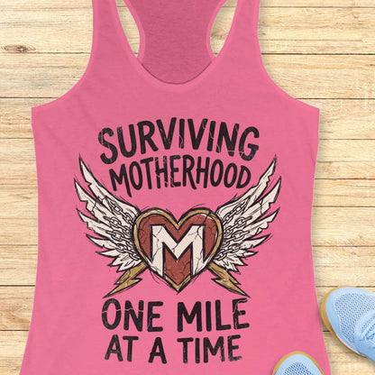 Pink tank top with 'Surviving Motherhood One Mile at a Time' text and heart design on a wooden surface.