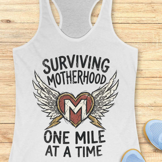 white tank top with 'Surviving Motherhood One Mile at a Time' text and heart design on a wooden surface.