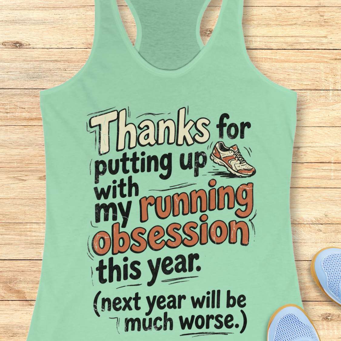 Light green tank top with humorous running text on a wooden surface