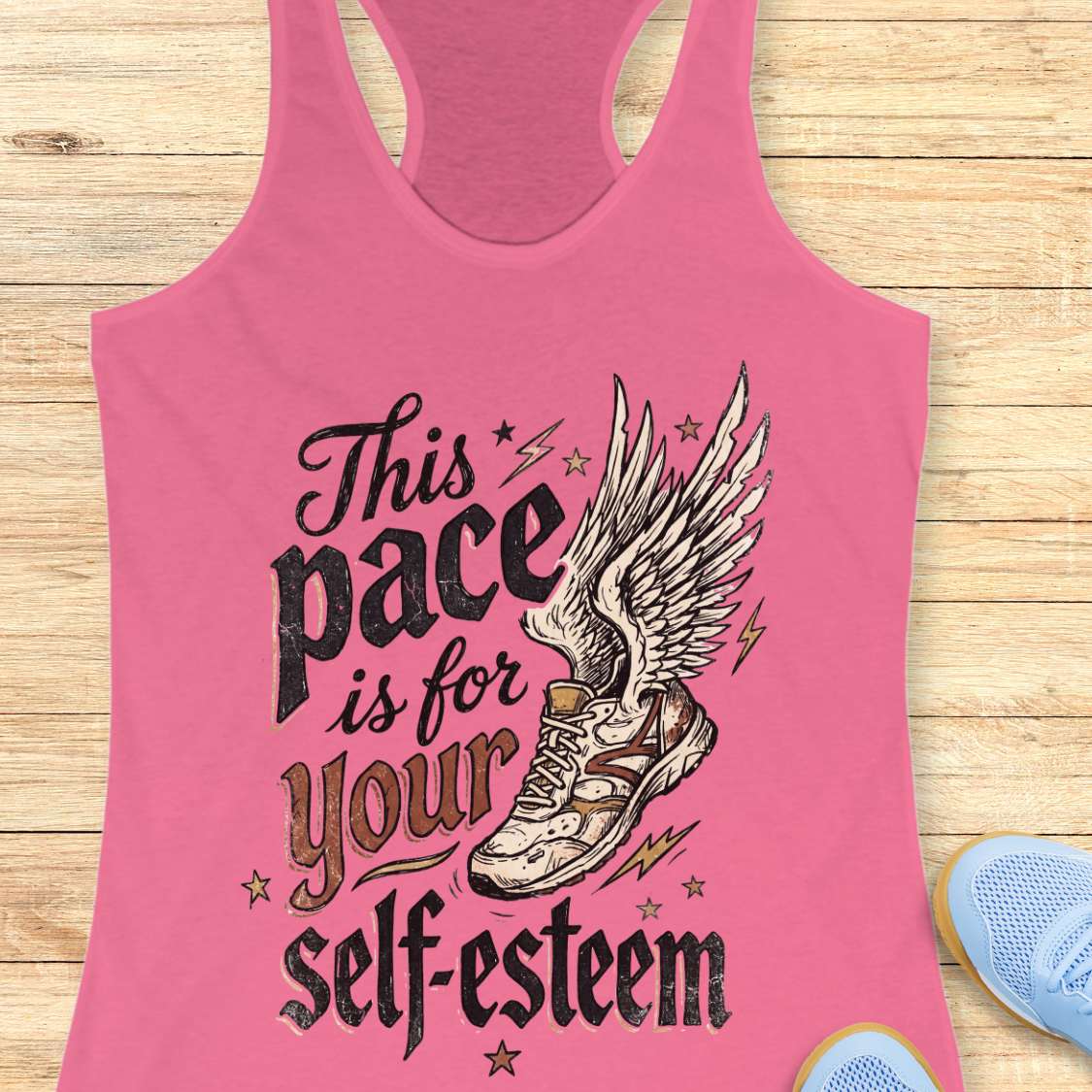 Pink tank top with motivational quote and shoe graphic on a wooden surface