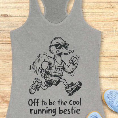 Gray tank top with a cartoon duck running and text 'Off to be the cool running bestie' on a wooden surface.