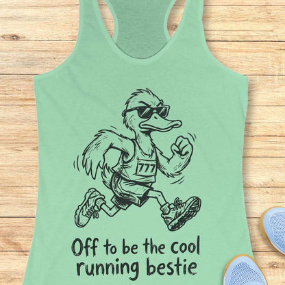 Mint green tank top with a cartoon ostrich running and sunglasses on, text 'Off to be the cool running bestie' on a wooden surface.