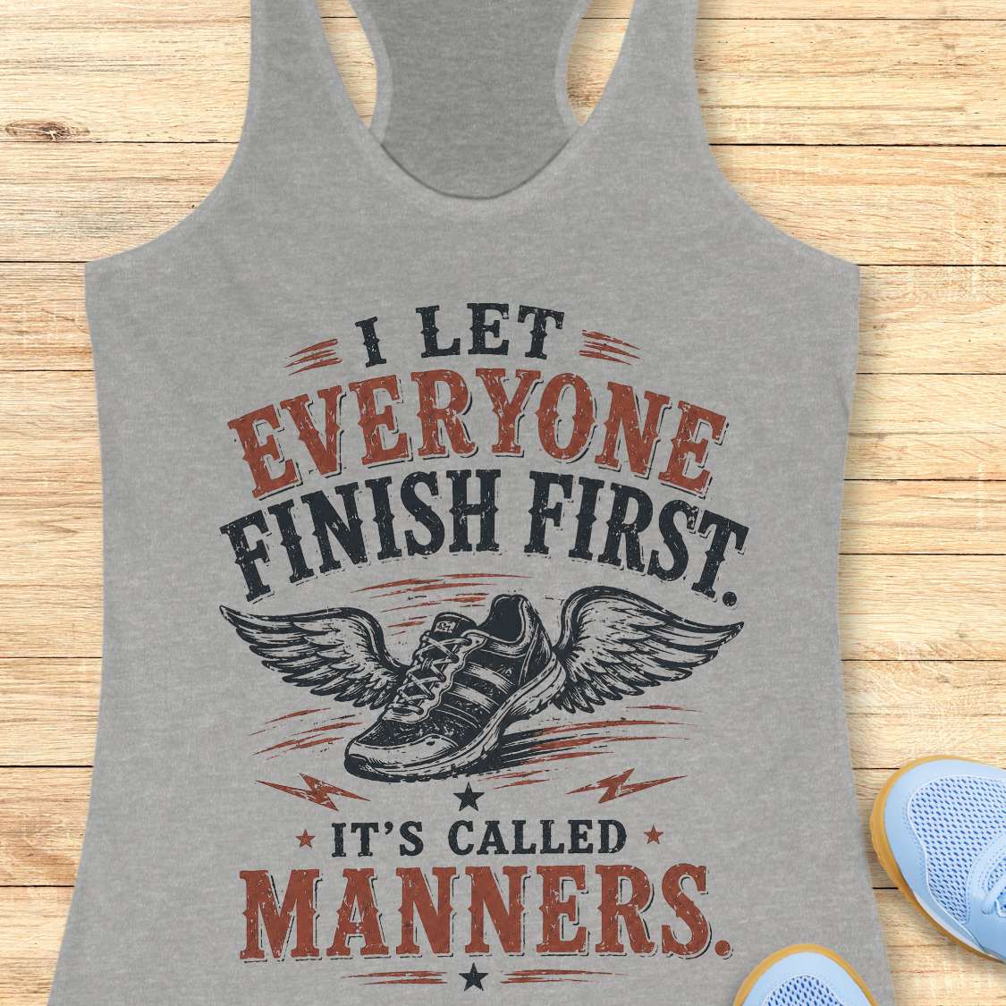 Gray tank top with motivational quote "I let everyone finish first. It's called manners." on a wooden surface