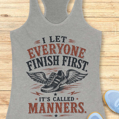 Gray tank top with motivational quote "I let everyone finish first. It's called manners." on a wooden surface