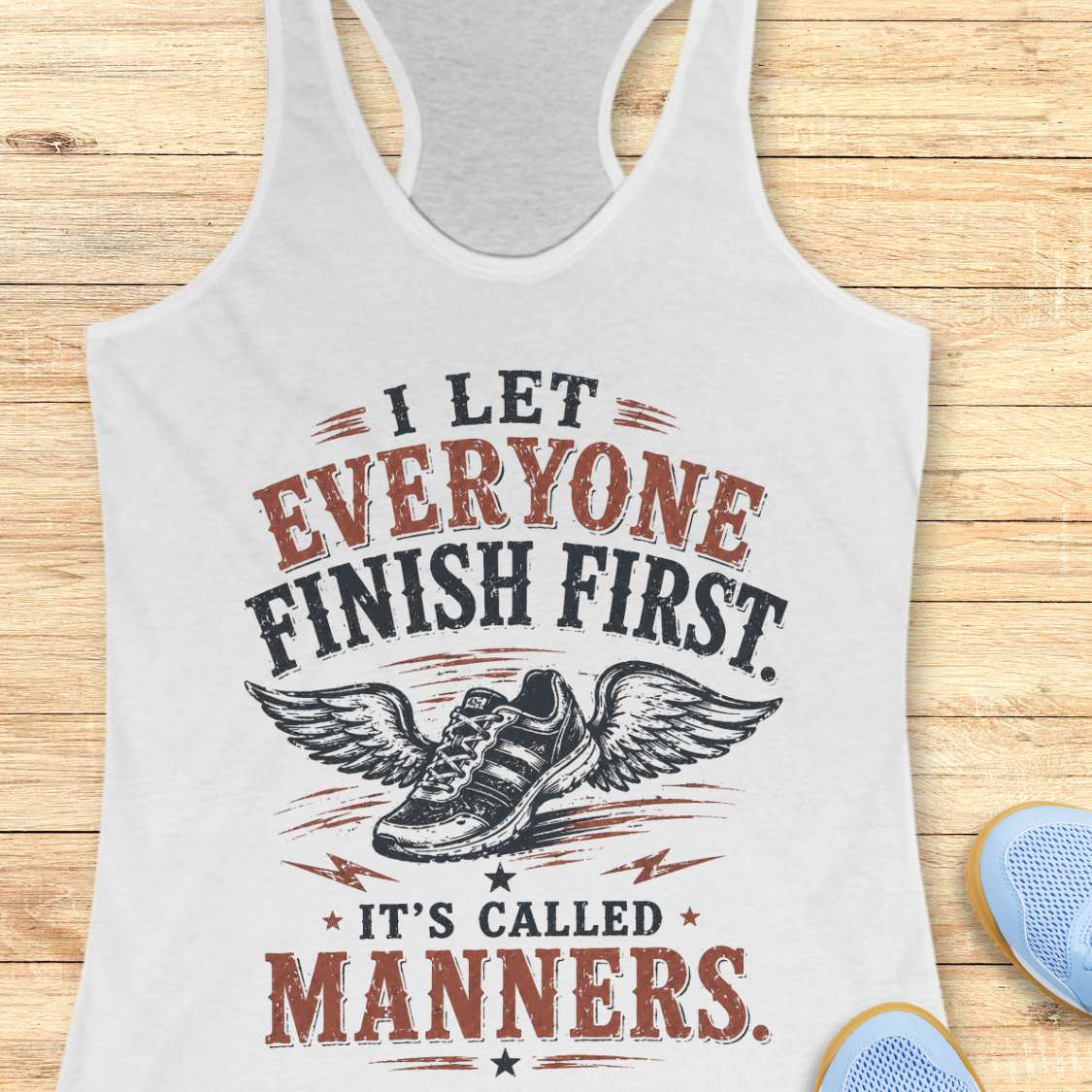 White tank top with a printed design and text - "I let everyone finish first. It's called manners."  on a wooden surface
