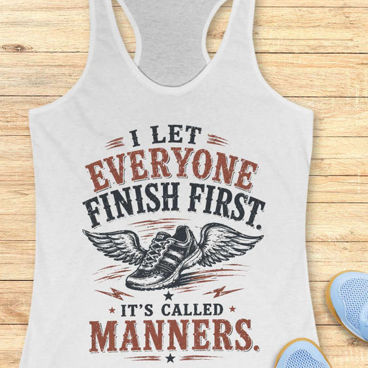 White tank top with a printed design and text - "I let everyone finish first. It's called manners."  on a wooden surface