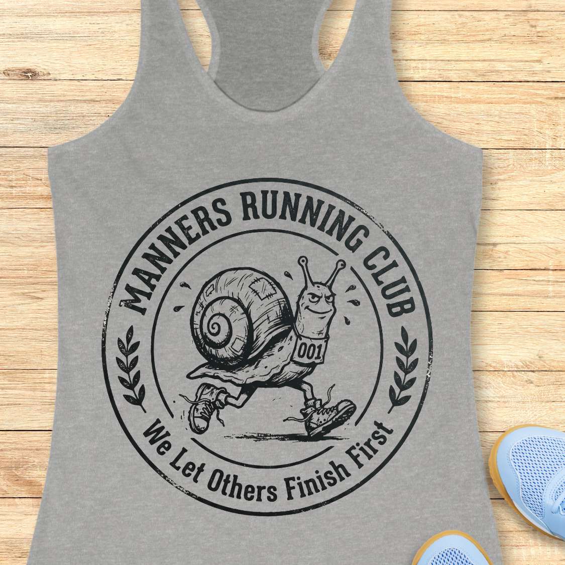 Gray tank top with 'Manners Running Club' graphic on a wooden surface
