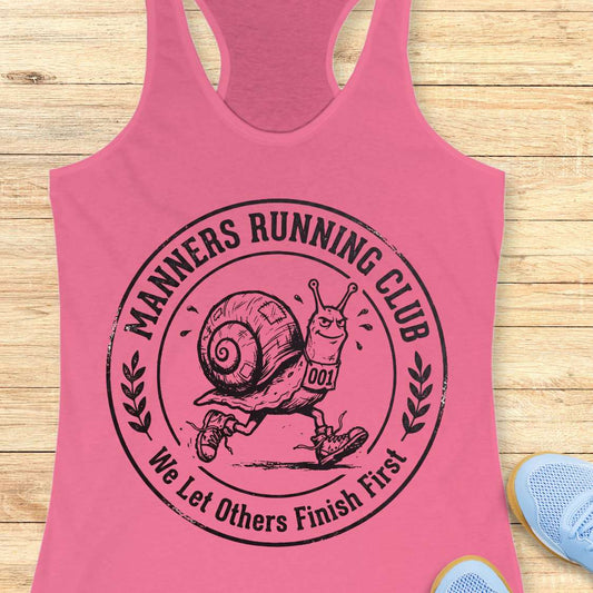 Pink tank top with 'Manners Running Club' graphic on a wooden surface