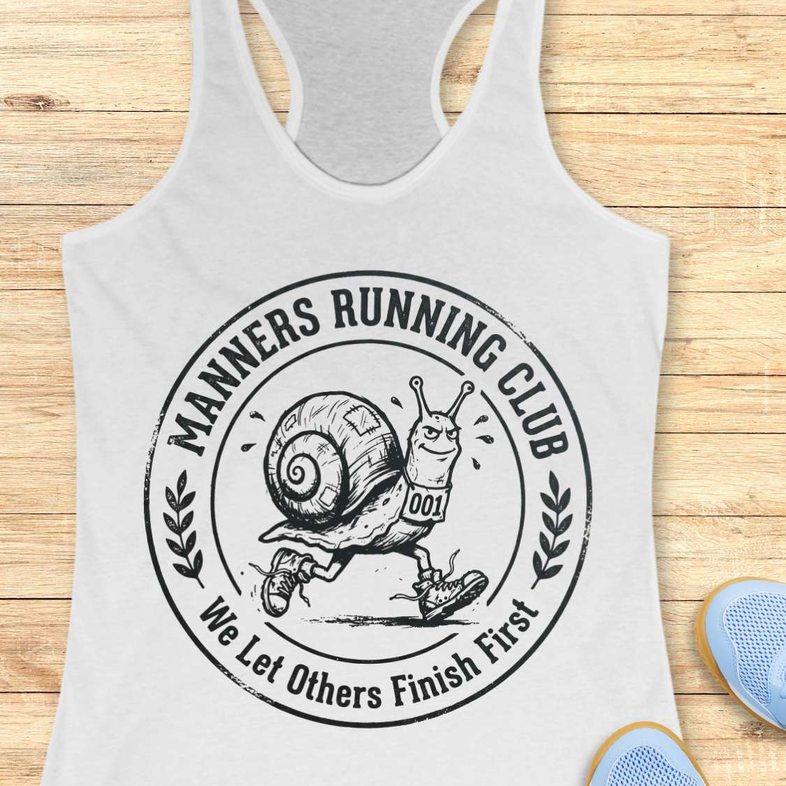 White tank top with 'Manners Running Club' graphic on a wooden surface