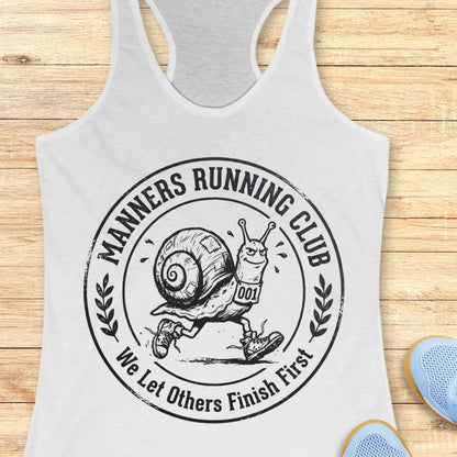 White tank top with 'Manners Running Club' graphic on a wooden surface