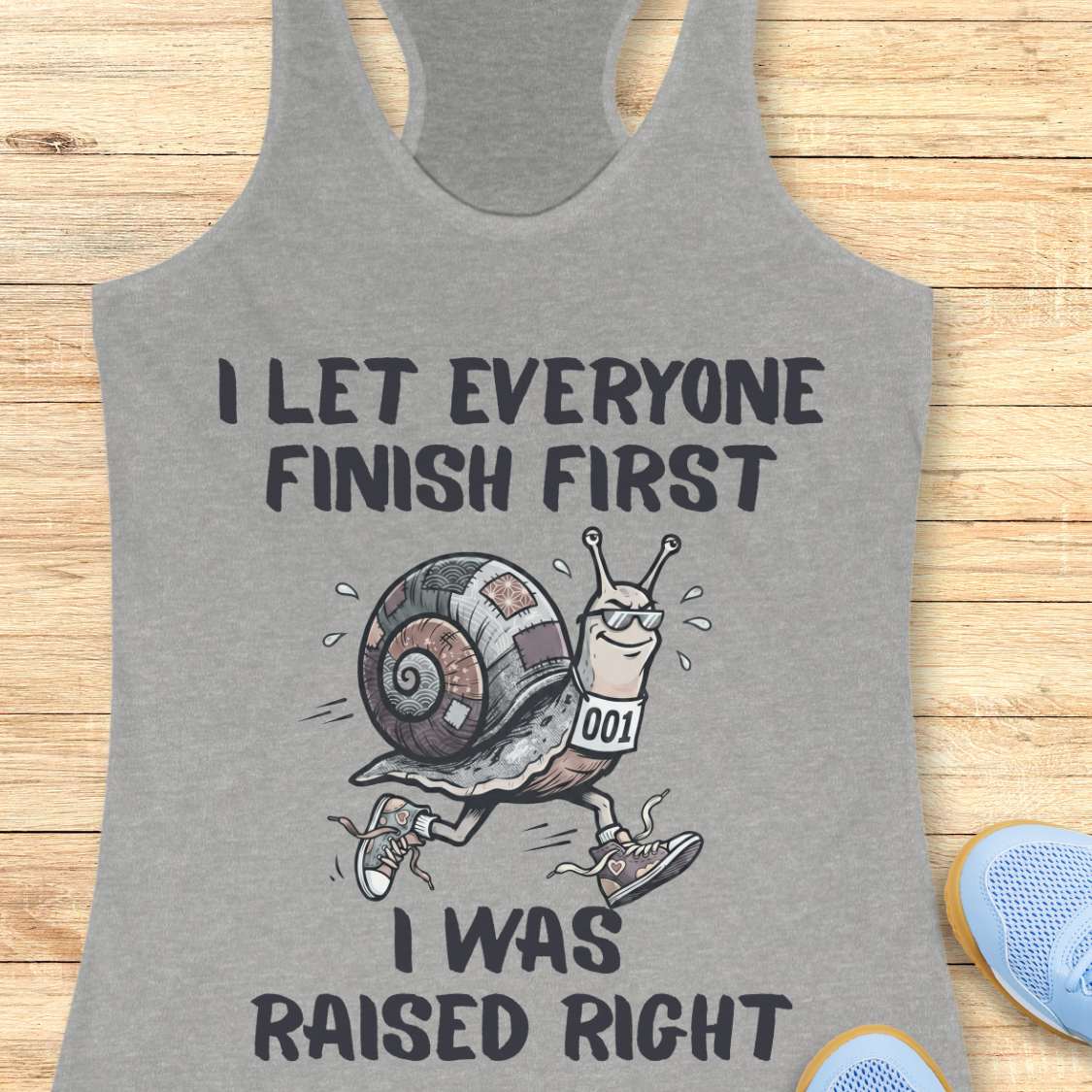 Gray tank top with a snail graphic and text I let everyone finish first I was raised right,  on a wooden surface