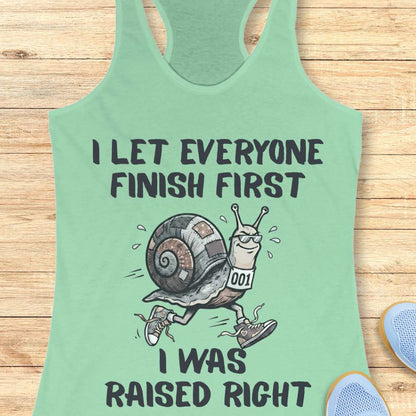 Mint green tank top with a snail graphic and text I let everyone finish first I was raised right,  on a wooden surface