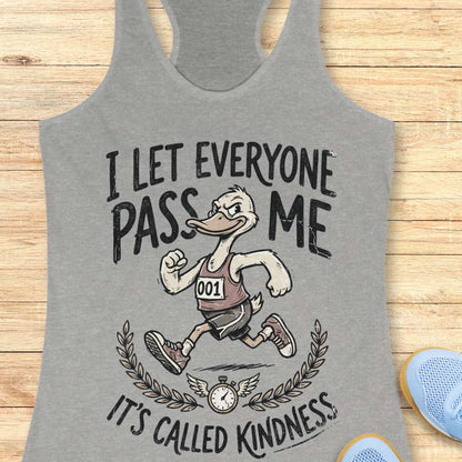 Gray tank top with a graphic of a running duck and text - I let everyone pass me, it's called kindness, on a wooden surface
