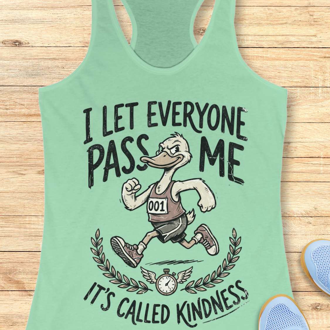 Mint green tank top with cartoon character and text I let everyone pass me, it's called kindness, on a wooden surface