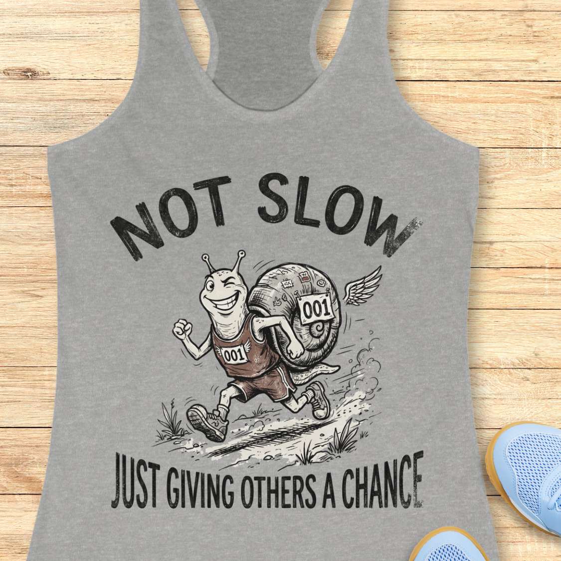 Gray tank top with a cartoon snail and text 'Not Slow Just Giving Others a Chance' on a wooden surface.
