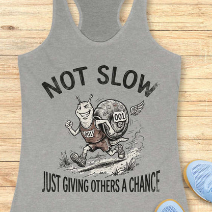 Gray tank top with a cartoon snail and text 'Not Slow Just Giving Others a Chance' on a wooden surface.