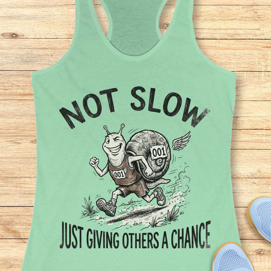 Mint green tank top with a snail graphic and text - not slow, just giving others a chance, on a wooden surface