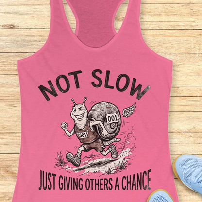 Pink tank top with a snail graphic and text - not slow, just giving others a chance, on a wooden surface