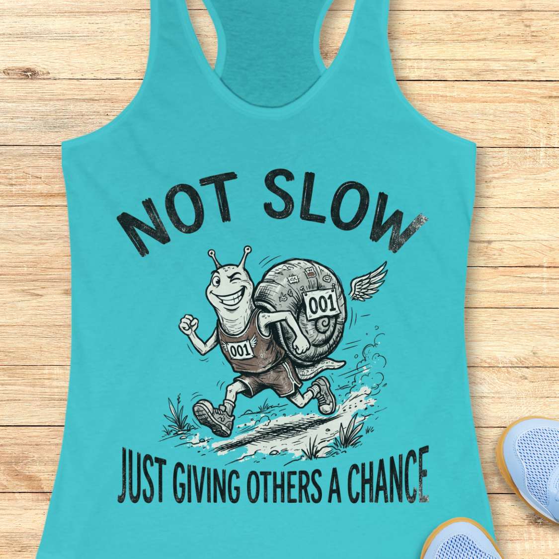 Turquoise tank top with a running snail graphic and text - not slow, just giving others a chance, on a wooden surface