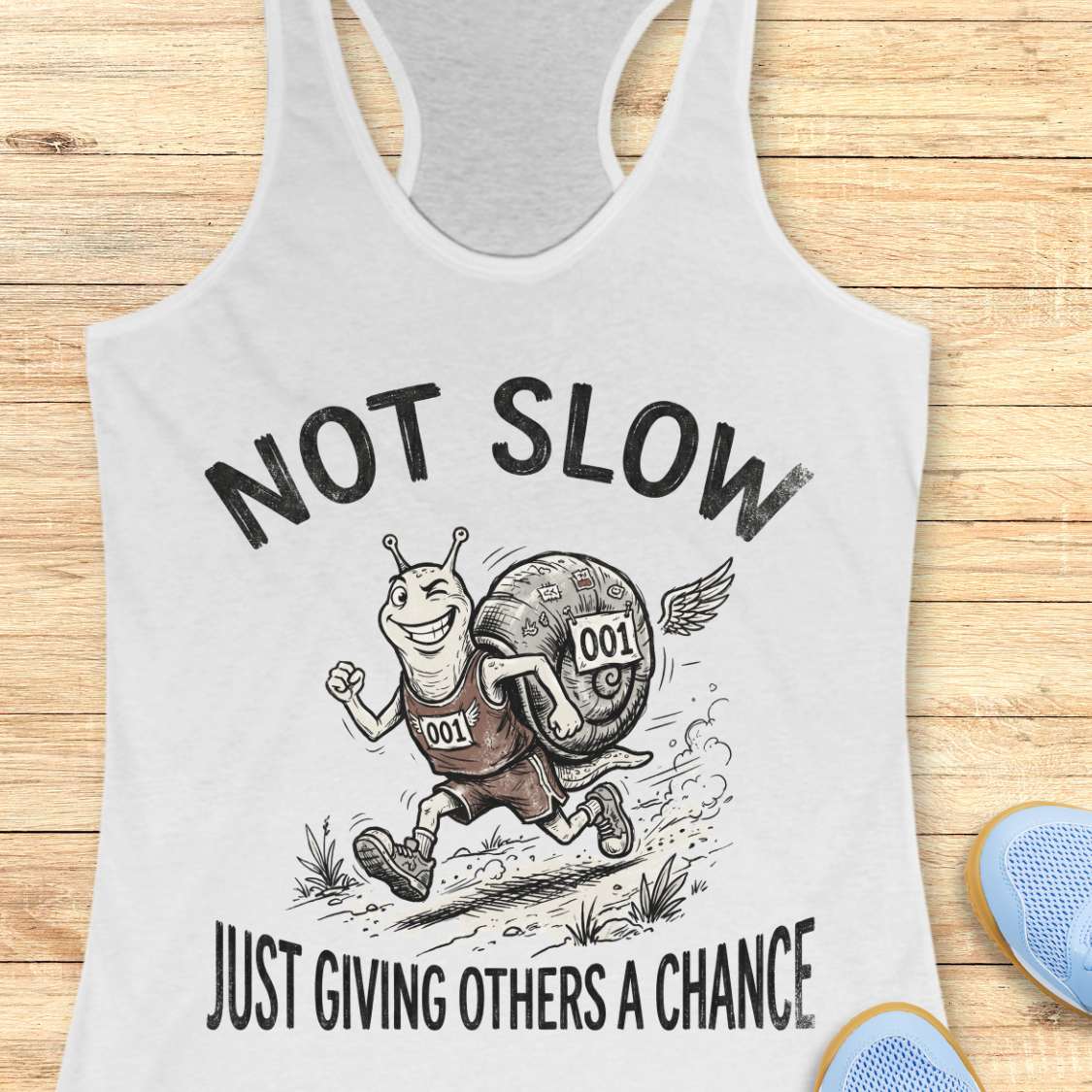 white tank top with a snail graphic and text - not slow, just giving others a chance, on a wooden surface