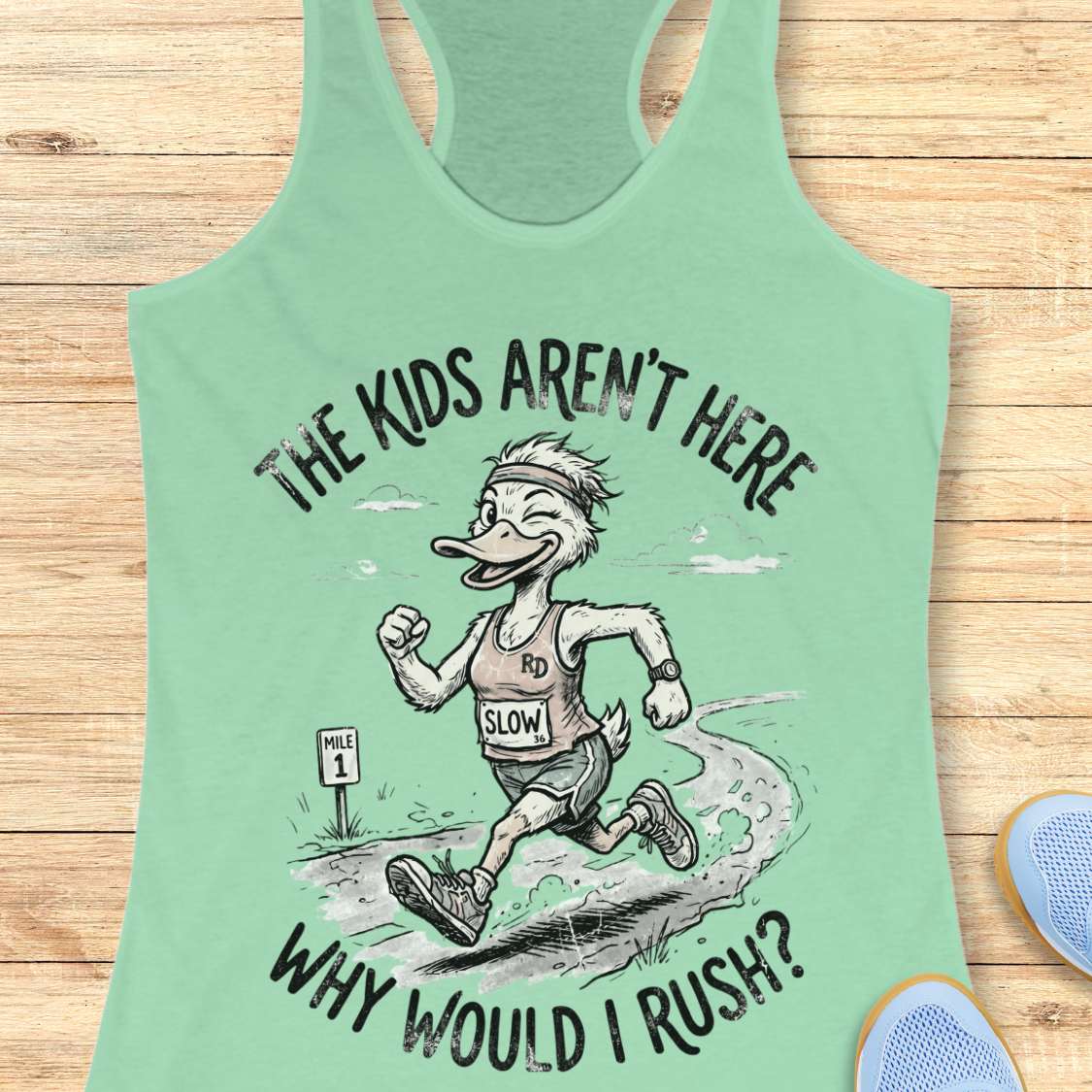 Mint green tank top with cartoon character and text - the kids aren't here, why would I rush?, on a wooden surface