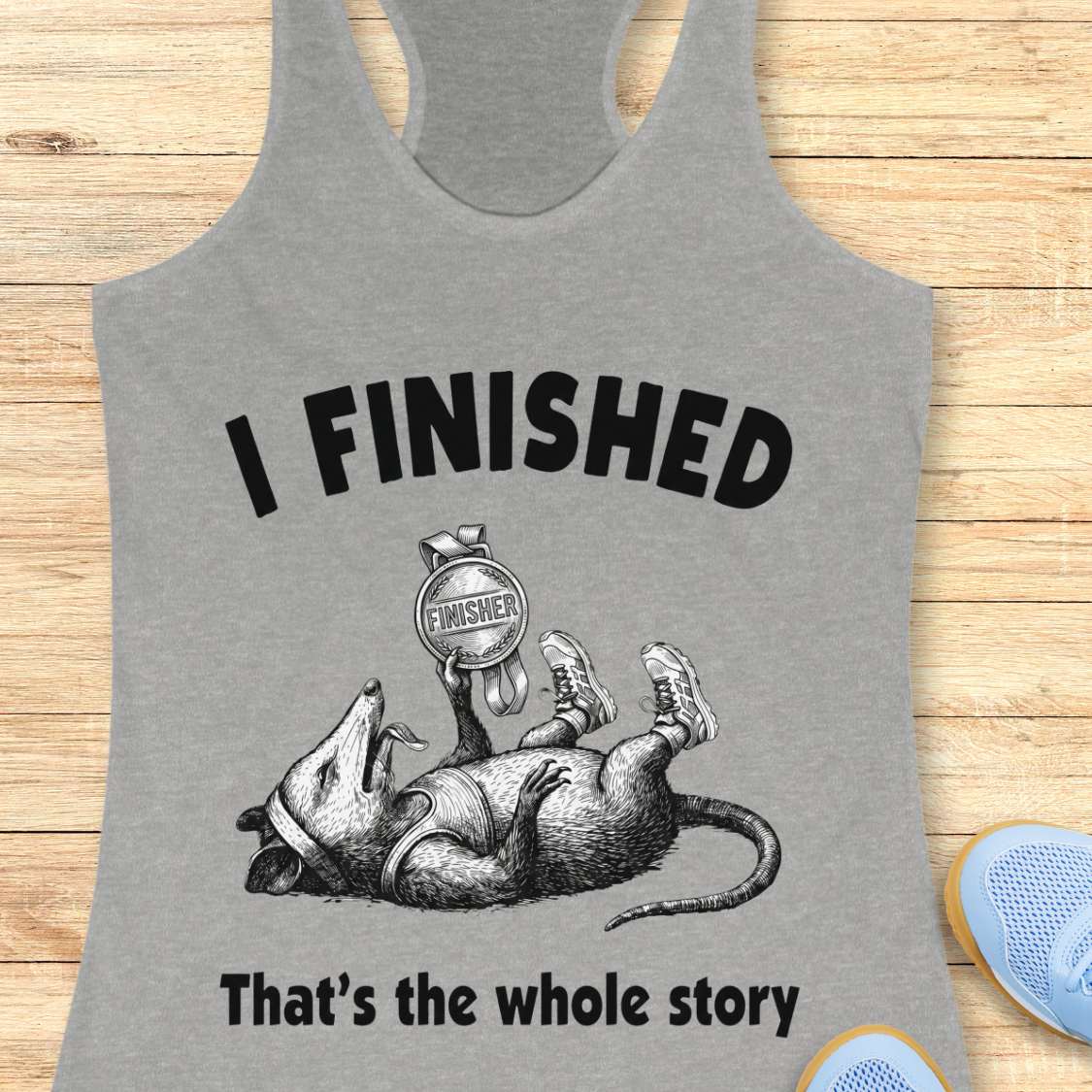 Gray tank top with graphic of a rat and text 'I FINISHED That's the whole story' on a wooden surface.