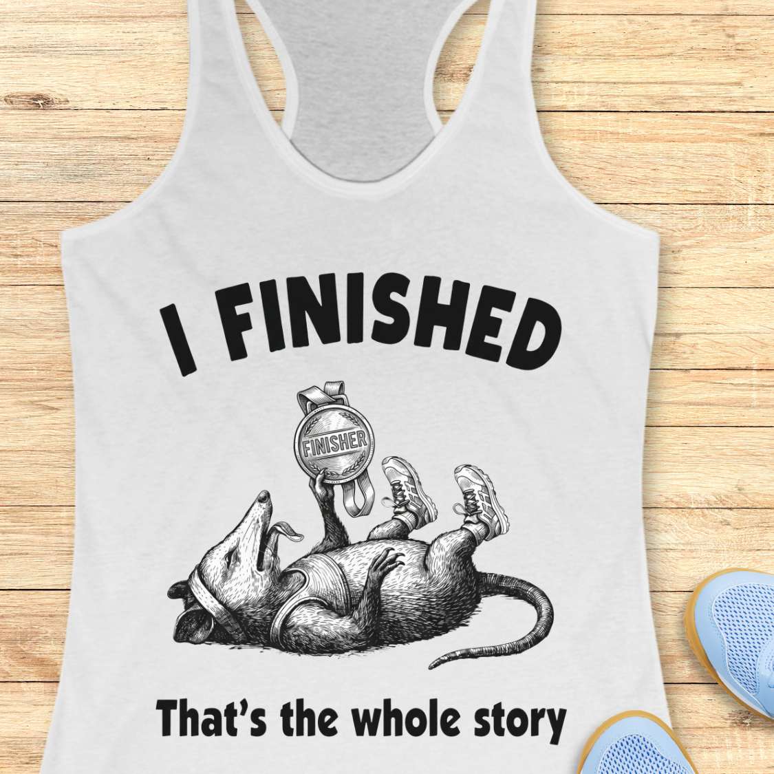 white tank top with graphic of a finished runner and text 'I FINISHED That's the whole story' on a wooden surface.