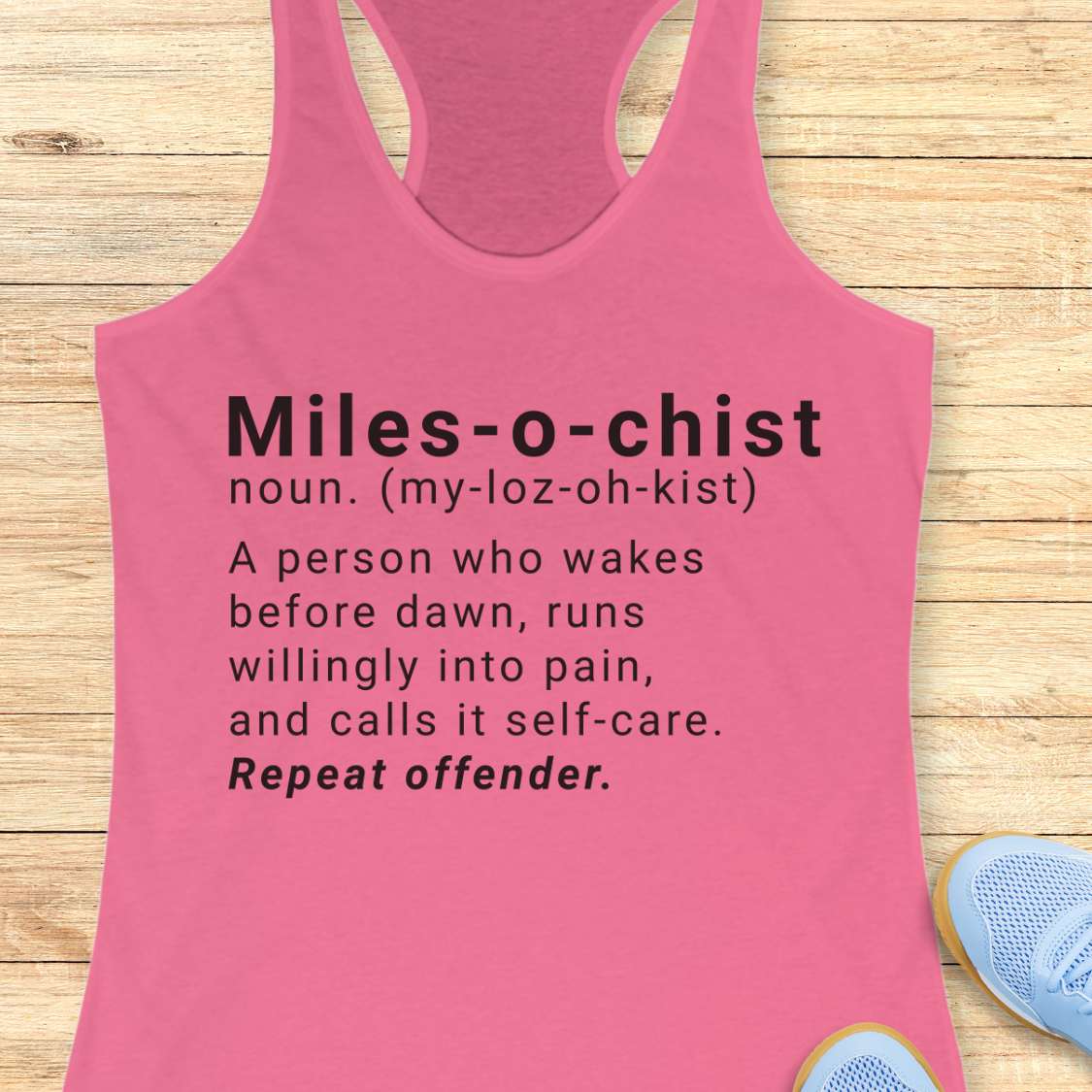 Pink tank top with humorous definition text on a wooden surface