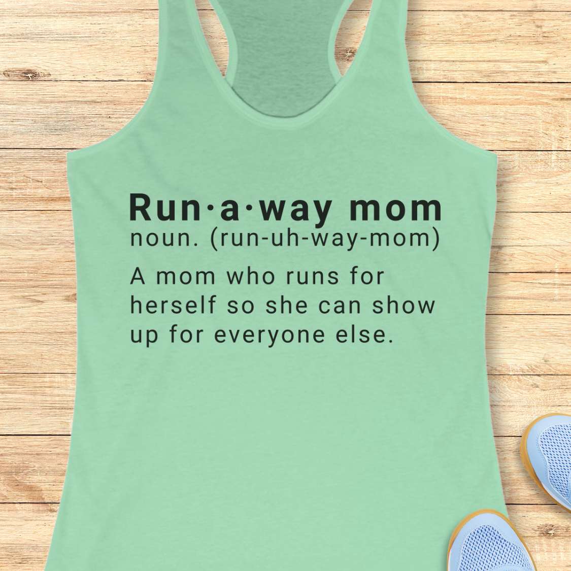 Green tank top with dictionary definition of run a way mom text on a wooden surface