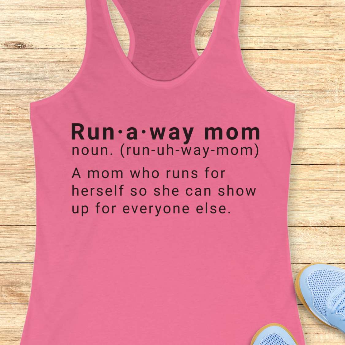 Pink tank top with dictionary definition of run a way mom text on a wooden surface