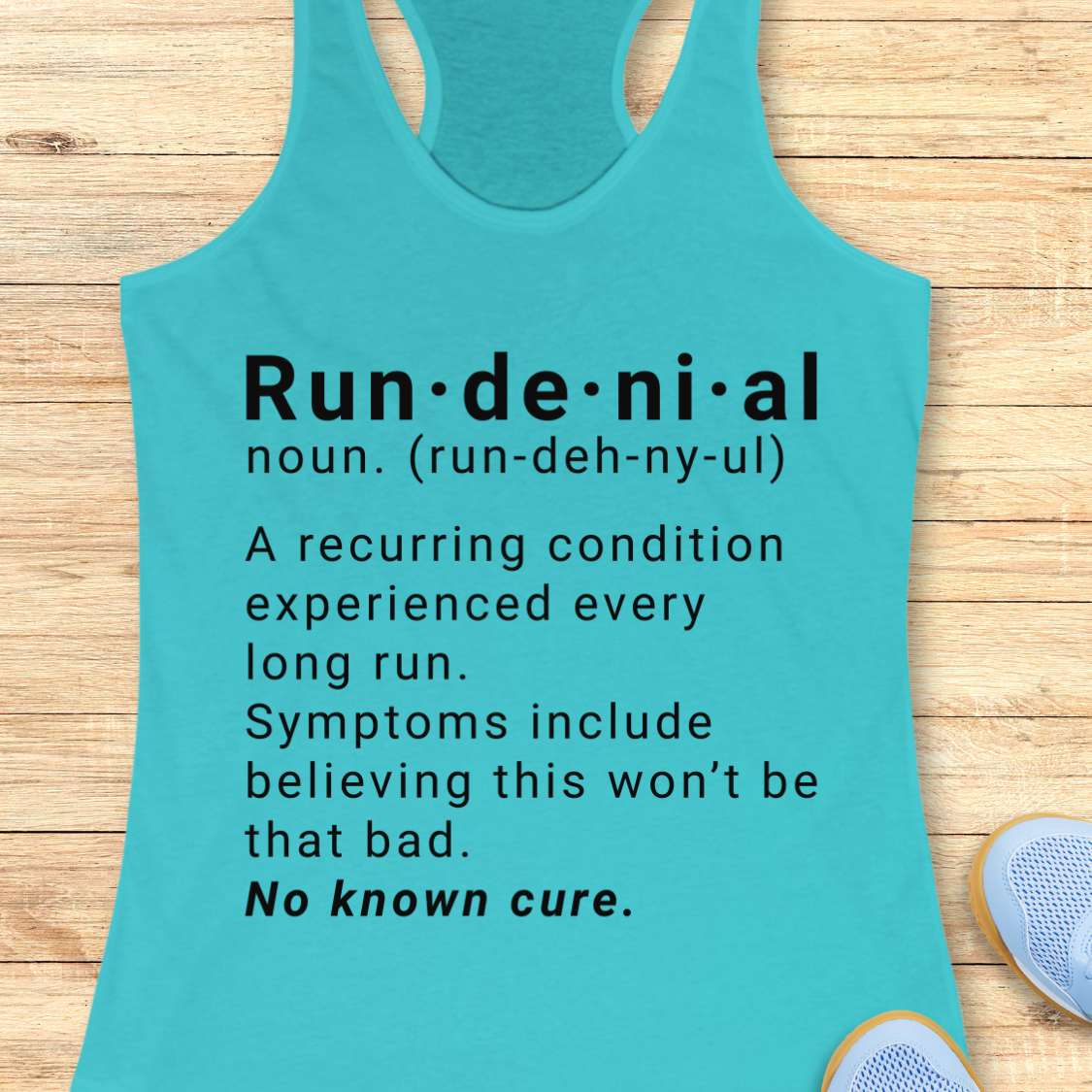 Turquoise tank top with humorous definition text  of run de ni al  on a wooden surface