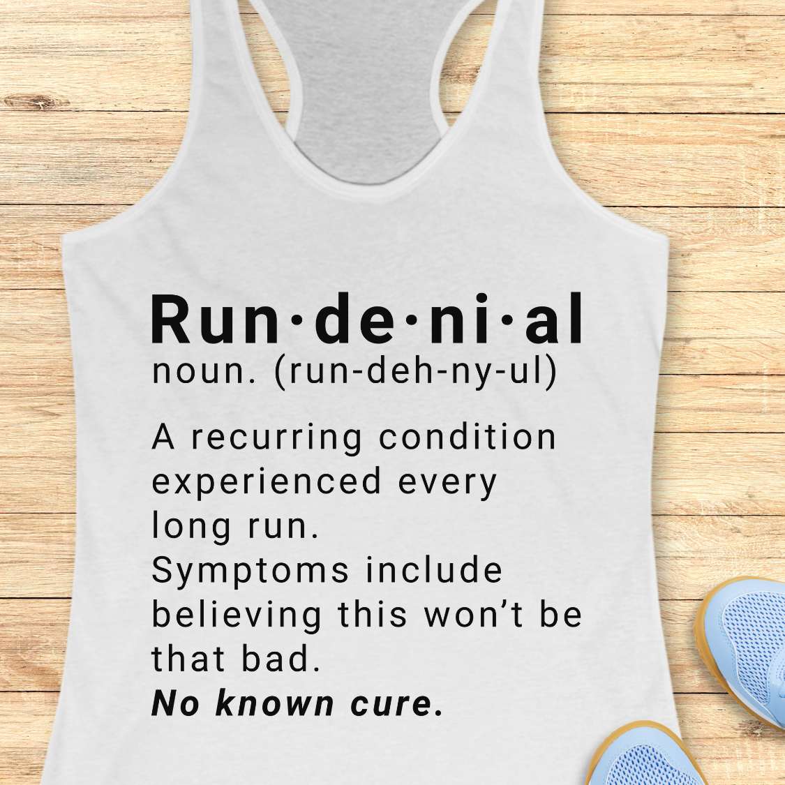 white tank top with humorous definition text  of run de ni al  on a wooden surface