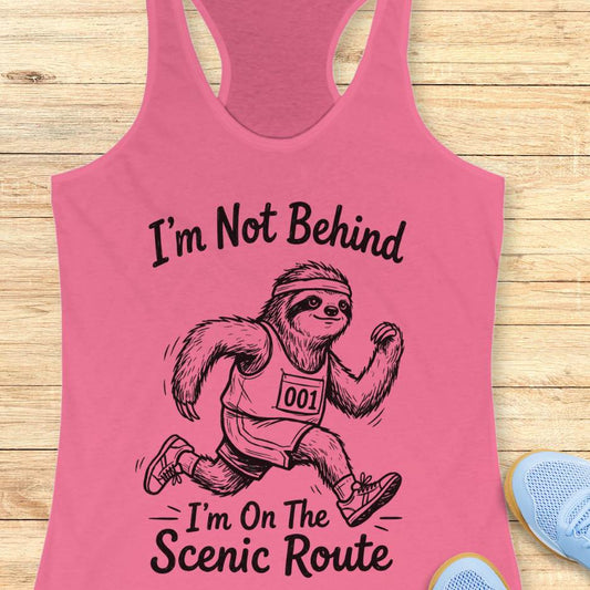 Pink tank top with a sloth graphic and text I'm not behind, I'm on the scenic route on a wooden surface