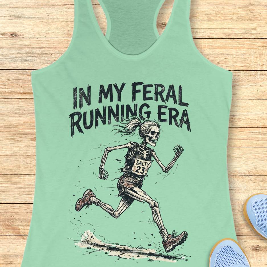 Mint green tank top with skeleton running graphic and text 'In my feral running era' on a wooden surface.
