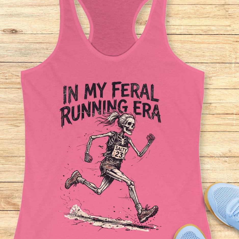 Pink tank top with skeleton runner graphic and text 'In my feral running era' on a wooden surface.