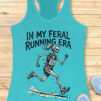 Turquoise tank top with skeleton running graphic and text 'In My Feral Running Era' on a wooden surface.