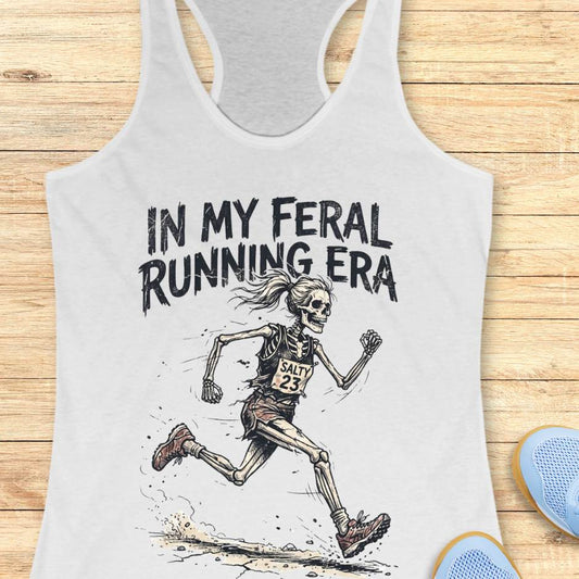 white Tank top with skeleton running graphic and text 'In my feral running era' on a wooden surface.