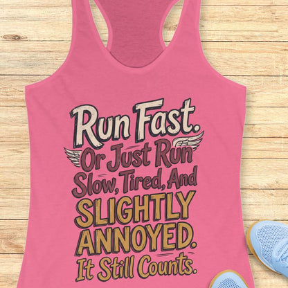 Pink tank top with humorous text "Run fast. Or just run slow, tired, and slightly annoyed. It still counts." on a wooden surface